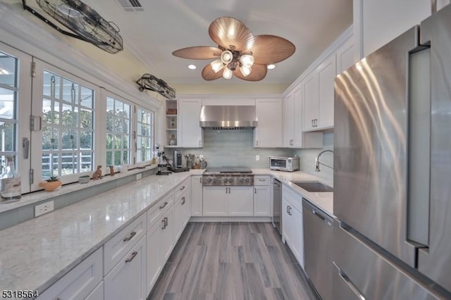 kitchen featuring light stone countertops, sink, wall chimney exhaust hood, white cabinets, and appliances with stainless steel finishes