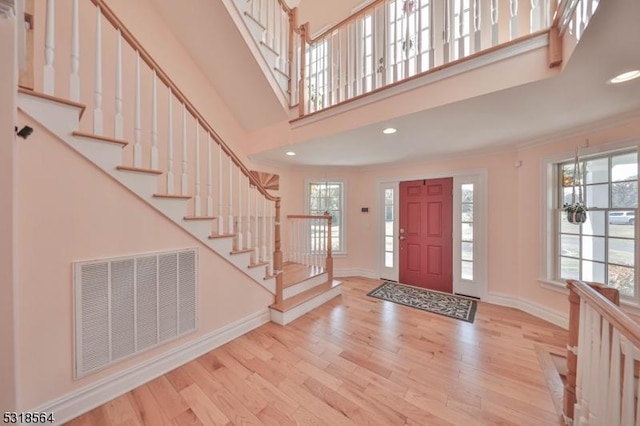 foyer entrance with an inviting chandelier, a towering ceiling, crown molding, and light hardwood / wood-style flooring