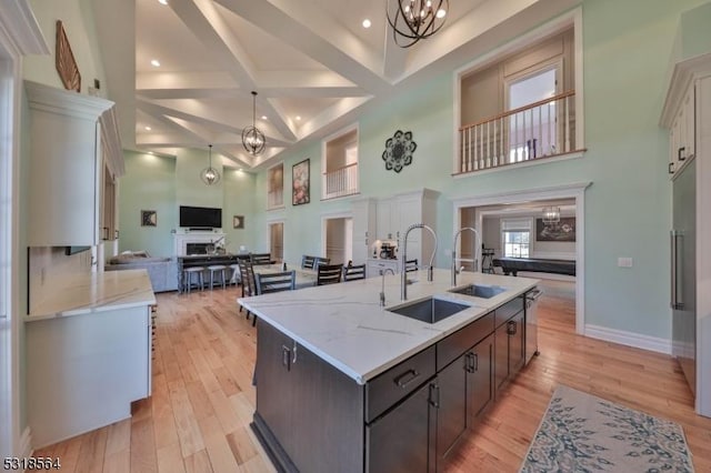 kitchen with dark brown cabinets, light stone countertops, light wood-type flooring, and a high ceiling