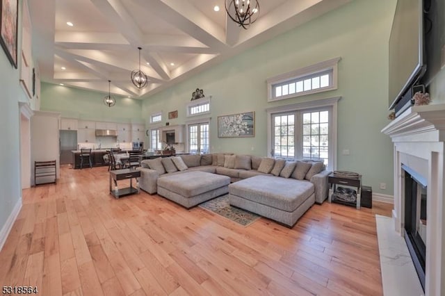 living room featuring a fireplace, french doors, a towering ceiling, and light hardwood / wood-style flooring