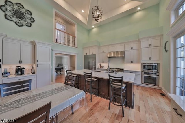 kitchen with a towering ceiling, stainless steel appliances, white cabinetry, and hanging light fixtures