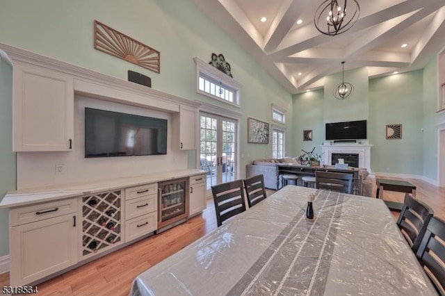 dining space featuring high vaulted ceiling, french doors, wine cooler, light wood-type flooring, and a notable chandelier