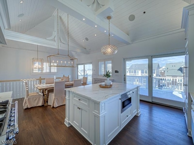 kitchen featuring stainless steel microwave, white cabinetry, beam ceiling, and hanging light fixtures