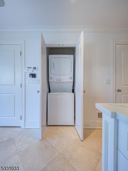 washroom featuring stacked washer and dryer, ornamental molding, and light tile patterned flooring