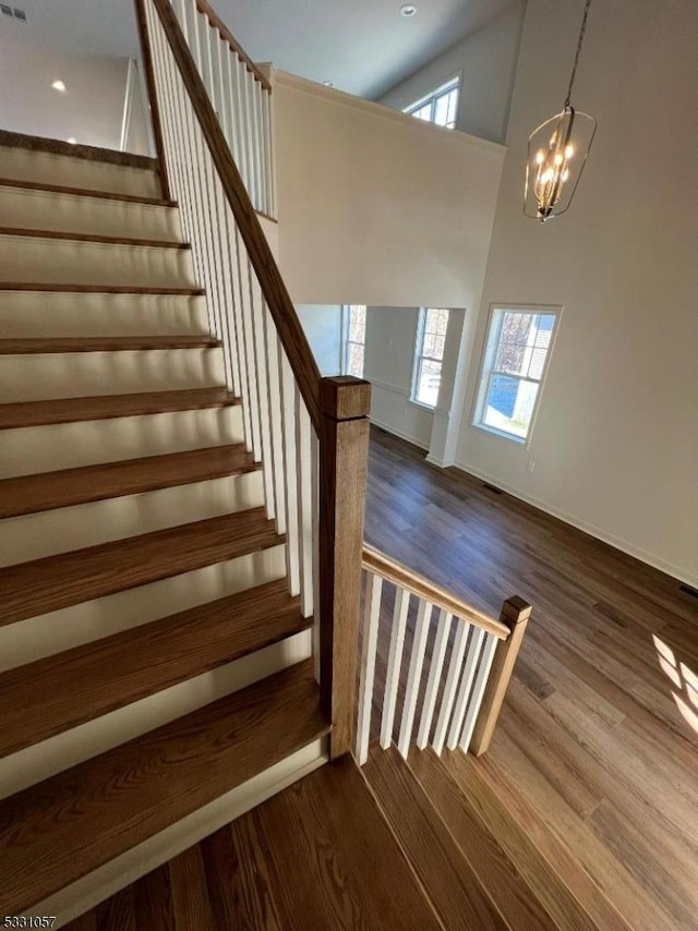 staircase featuring a notable chandelier, plenty of natural light, a towering ceiling, and hardwood / wood-style flooring