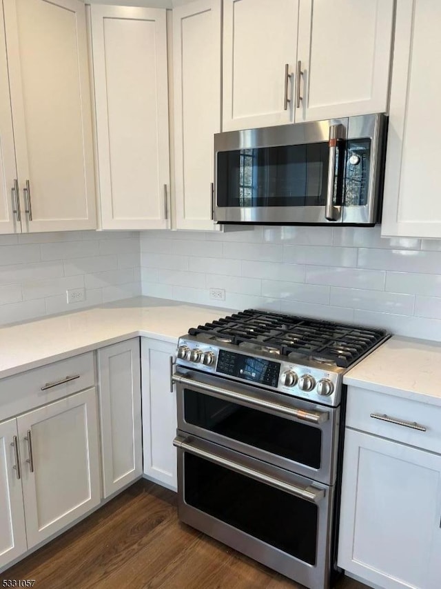 kitchen with backsplash, dark hardwood / wood-style flooring, white cabinets, and stainless steel appliances