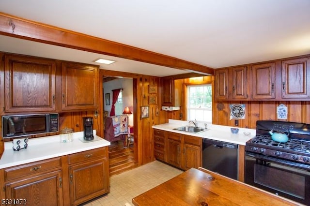 kitchen with black appliances, beam ceiling, sink, and wooden walls