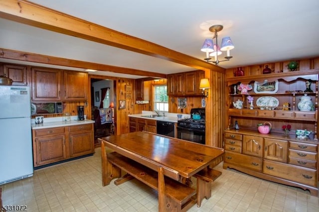 kitchen with wooden walls, sink, black appliances, beamed ceiling, and hanging light fixtures