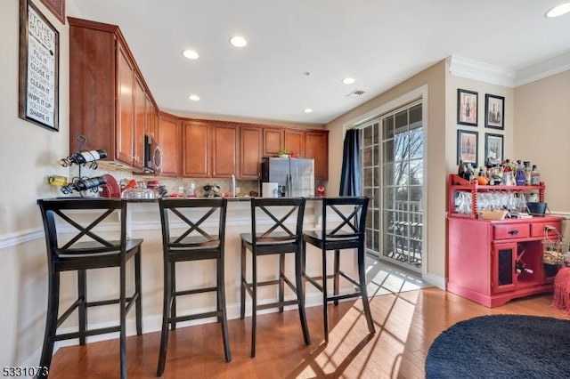 kitchen featuring a kitchen bar, backsplash, ornamental molding, stainless steel appliances, and light hardwood / wood-style floors