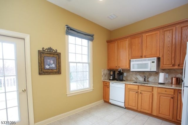 kitchen with backsplash, light stone countertops, sink, and white appliances