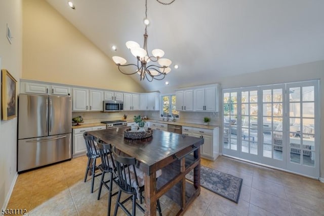 kitchen featuring high vaulted ceiling, appliances with stainless steel finishes, light tile patterned floors, and white cabinetry