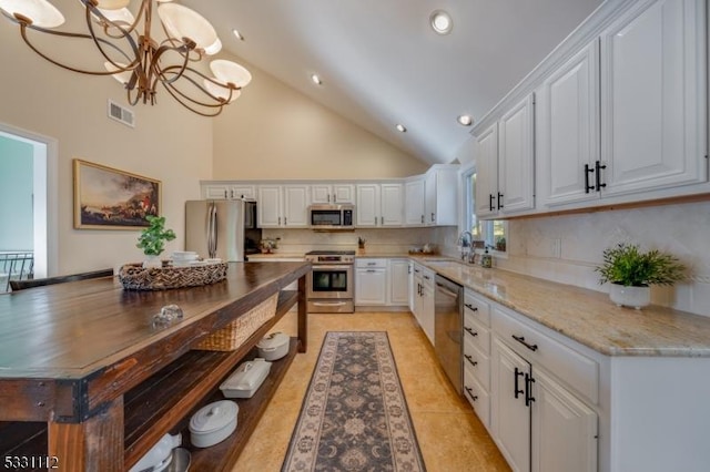 kitchen featuring high vaulted ceiling, white cabinetry, hanging light fixtures, and appliances with stainless steel finishes