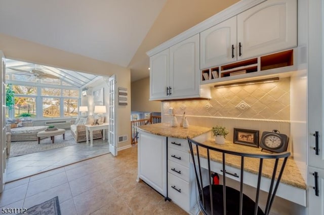 kitchen with lofted ceiling, white cabinetry, tasteful backsplash, and light stone counters