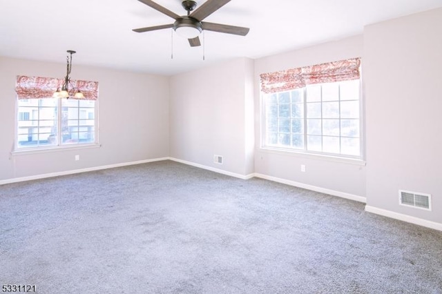 carpeted spare room featuring ceiling fan with notable chandelier