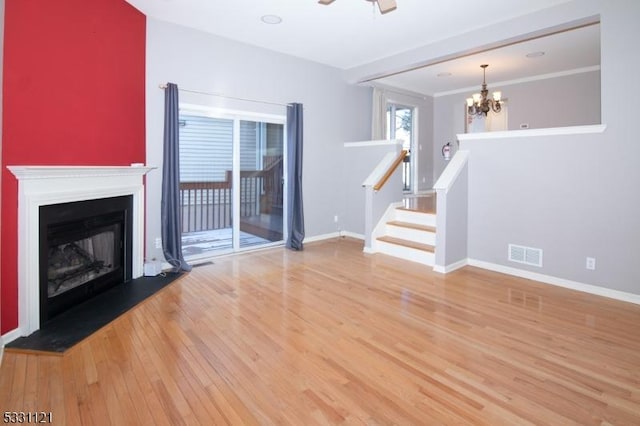 unfurnished living room with hardwood / wood-style floors, ceiling fan with notable chandelier, and crown molding