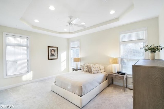 carpeted bedroom featuring multiple windows, a tray ceiling, and ceiling fan