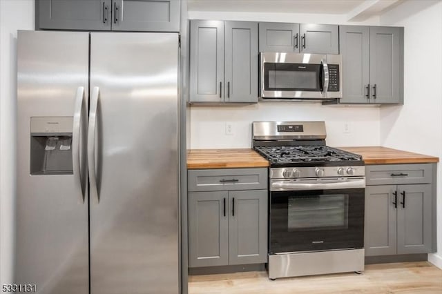 kitchen with gray cabinetry, light hardwood / wood-style flooring, wooden counters, and appliances with stainless steel finishes