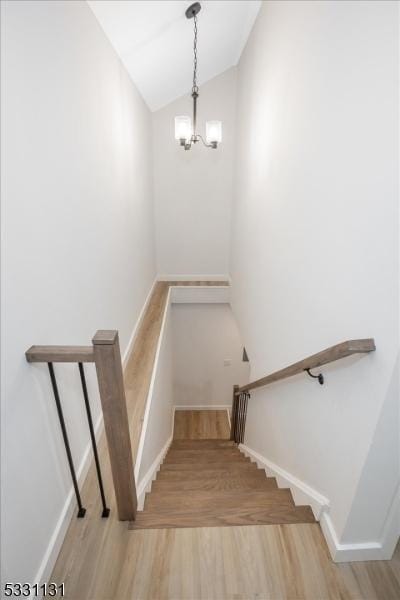 staircase featuring hardwood / wood-style flooring, vaulted ceiling, and an inviting chandelier