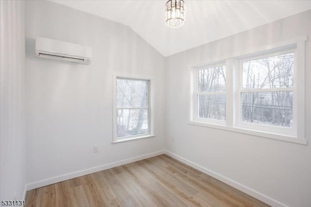 spare room with light wood-type flooring, an AC wall unit, lofted ceiling, and a notable chandelier