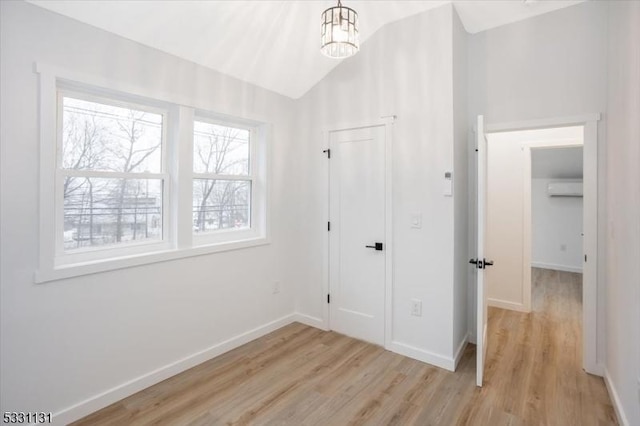 unfurnished bedroom with a notable chandelier, vaulted ceiling, light hardwood / wood-style flooring, and a wall mounted AC