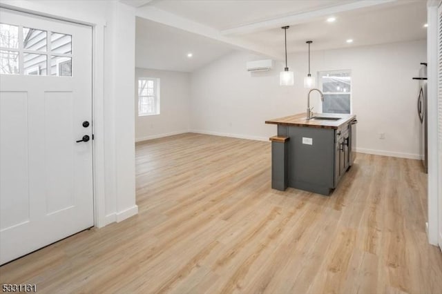 kitchen with pendant lighting, sink, light wood-type flooring, a wall mounted AC, and butcher block counters