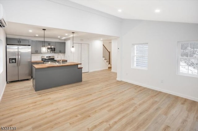 kitchen with butcher block counters, decorative light fixtures, gray cabinets, appliances with stainless steel finishes, and light wood-type flooring