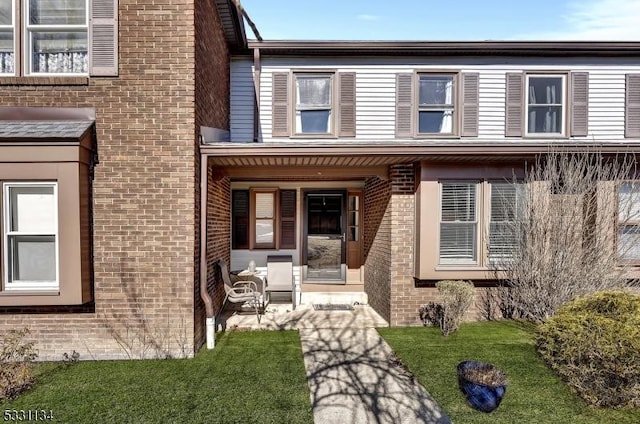 townhome / multi-family property featuring brick siding, a front lawn, and a porch