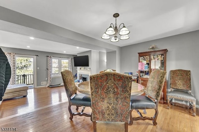 dining area featuring light wood-style floors, a fireplace, baseboards, and a notable chandelier