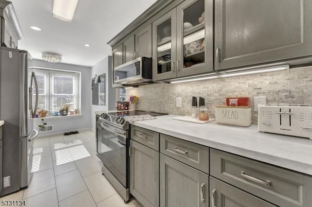 kitchen featuring appliances with stainless steel finishes, light countertops, gray cabinets, backsplash, and light tile patterned flooring