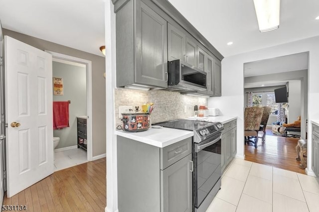 kitchen featuring electric range oven, stainless steel microwave, gray cabinets, light countertops, and backsplash