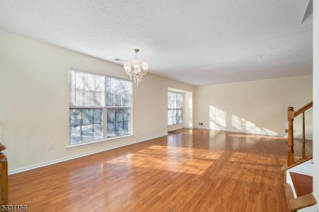 unfurnished living room featuring hardwood / wood-style flooring, a textured ceiling, and a notable chandelier