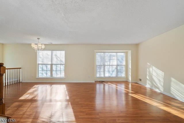 unfurnished room featuring hardwood / wood-style floors, a textured ceiling, and a chandelier