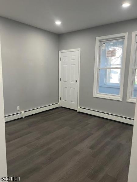 unfurnished room featuring a baseboard heating unit and dark hardwood / wood-style floors