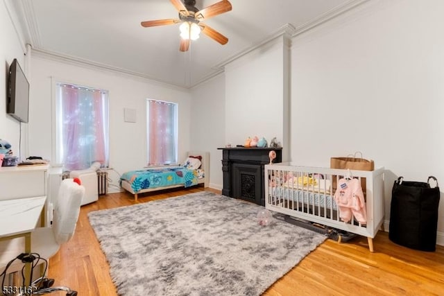 bedroom featuring hardwood / wood-style floors, ceiling fan, a crib, and crown molding