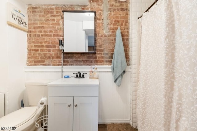 bathroom with a shower with curtain, vanity, toilet, and brick wall