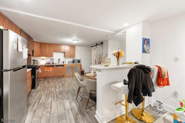 kitchen with light wood-type flooring, appliances with stainless steel finishes, and a barn door