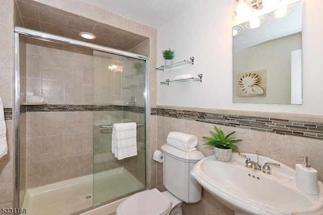 full bath featuring wainscoting, toilet, a sink, a shower stall, and tile walls