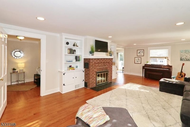 living room featuring a brick fireplace, crown molding, wood finished floors, and recessed lighting