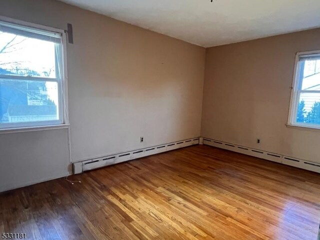 spare room featuring wood-type flooring, a wealth of natural light, and a baseboard heating unit