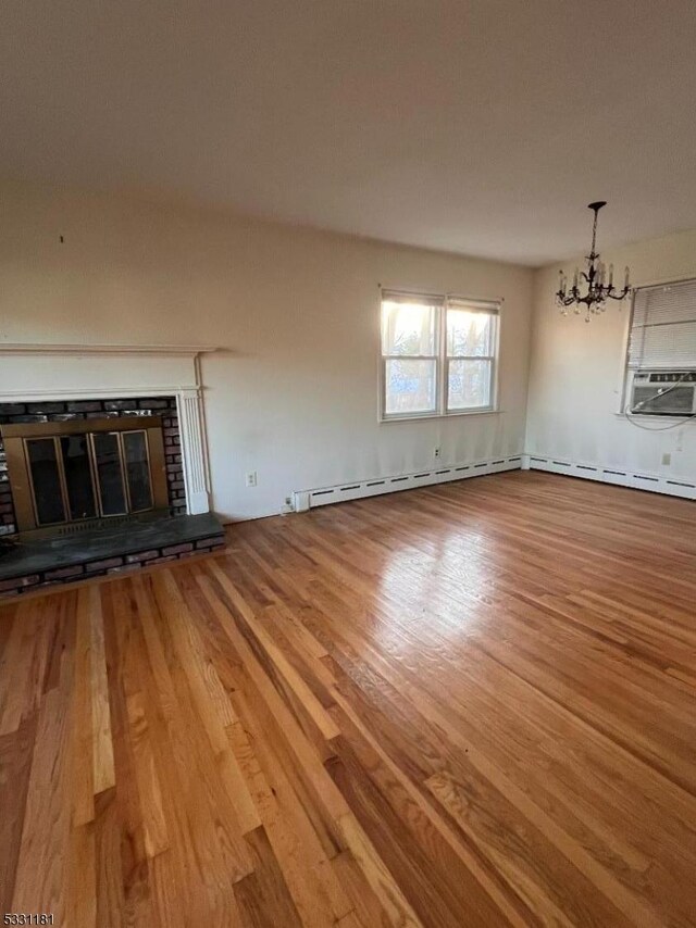 unfurnished living room featuring cooling unit, a fireplace, baseboard heating, a notable chandelier, and wood-type flooring