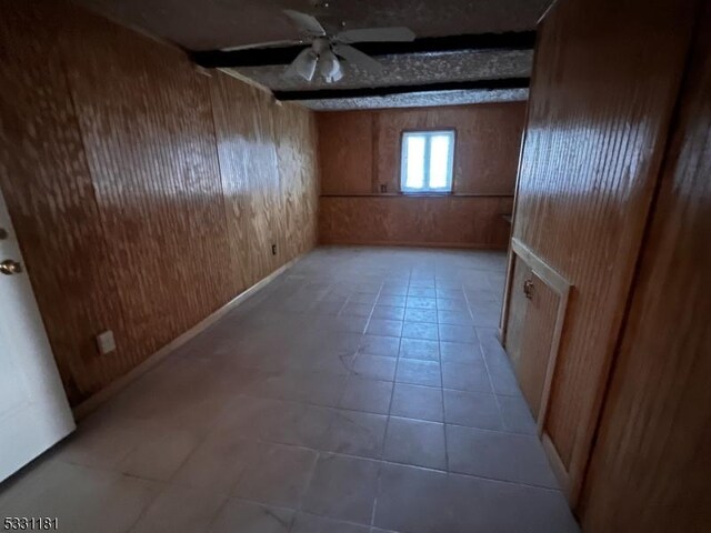 tiled spare room featuring ceiling fan and wood walls