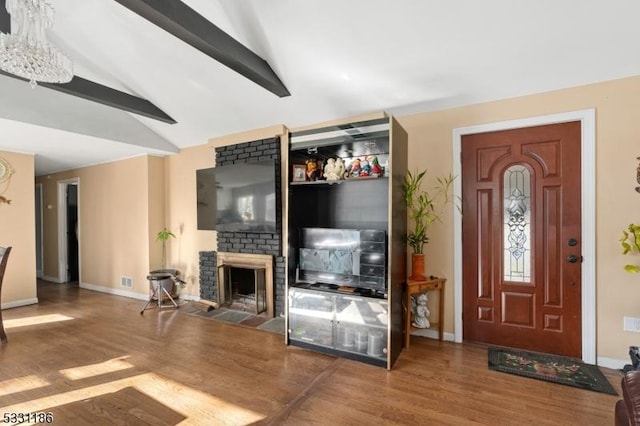 living room with hardwood / wood-style floors, vaulted ceiling with beams, an inviting chandelier, and a brick fireplace