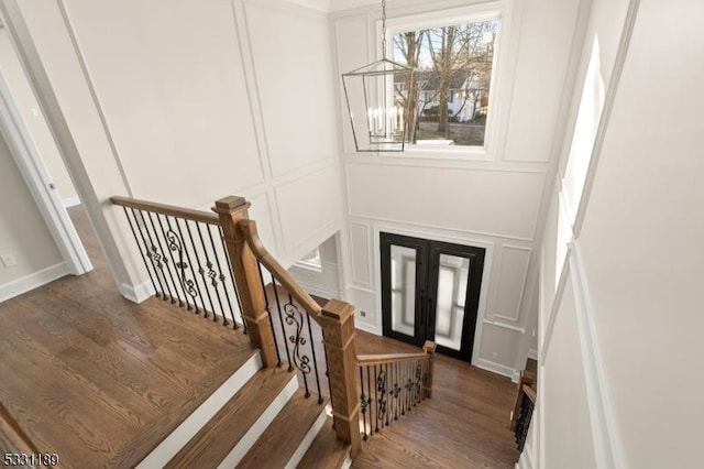 foyer featuring french doors, an inviting chandelier, wood finished floors, and a decorative wall