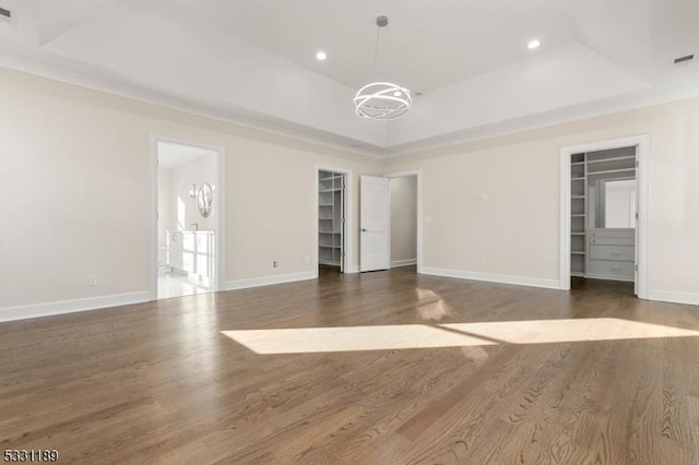 unfurnished bedroom with a walk in closet, baseboards, a tray ceiling, and wood finished floors