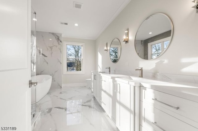 bathroom featuring marble finish floor, double vanity, visible vents, ornamental molding, and a freestanding tub