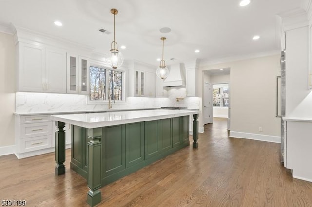 kitchen featuring light countertops, green cabinets, white cabinetry, premium range hood, and a kitchen breakfast bar