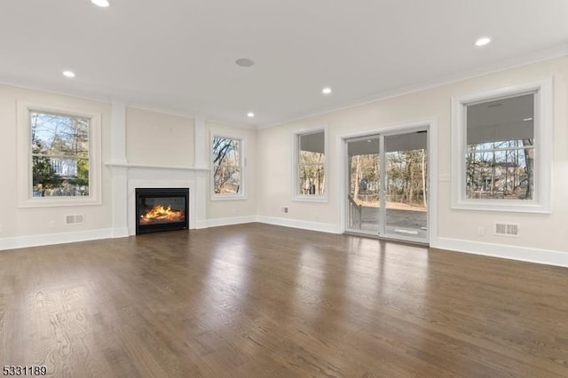 unfurnished living room with baseboards, dark wood finished floors, a wealth of natural light, and a glass covered fireplace