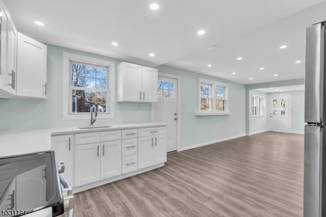 kitchen with white cabinetry, electric stove, stainless steel refrigerator, light hardwood / wood-style flooring, and sink