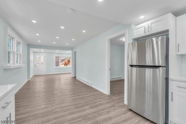 kitchen featuring a baseboard radiator, white cabinetry, light hardwood / wood-style floors, stainless steel refrigerator, and light stone counters