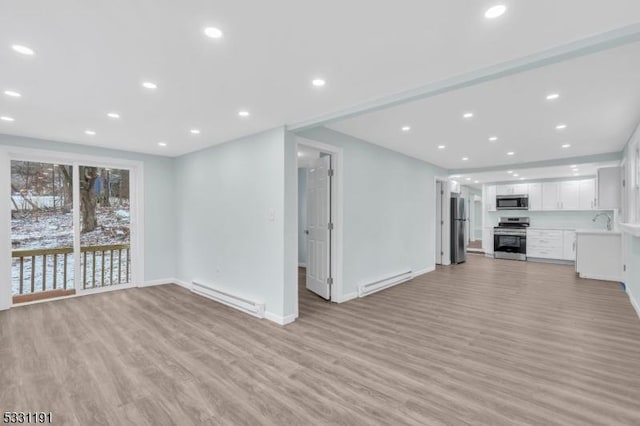 unfurnished living room featuring a baseboard heating unit, sink, and light hardwood / wood-style flooring